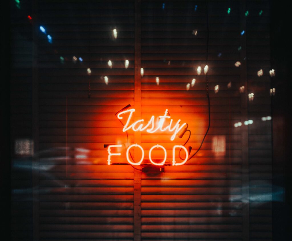 Neon sign reading “Tasty Food” glowing in a restaurant window, symbolizing New Orleans Restaurant Roulette and COOLinary 2025 dining choices.