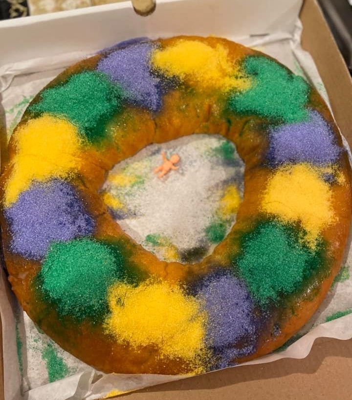 A traditional New Orleans king cake with purple, green, and gold sugar and a plastic baby in the center, representing brand consistency and Mardi Gras tradition.